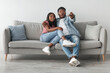 © Prostock-studio - Wow, Omg. Portrait of emotional excited African American couple watching TV show or movie with open mouth, hugging sitting on couch. Shocked guy holding remote control, family hearing breaking news