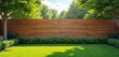 © Pete - Modern wooden fence provides privacy for a sunny backyard with vibrant green lawn. Lush garden beds and shade trees thrive, creating a peaceful outdoor home space under a clear blue sky.