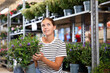 © JackF - Girl customer-onlooker curiously examines showcase exhibition with indoor evergreens flowering hebe. Owner of offline flower shop inspects showcase with goods new arrival