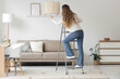 © Pixel-Shot - Young woman climbing stepladder near lamp in living room, back view