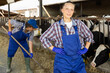 © JackF - Female farmer in blue overalls standing in cowshed in front of farmer with pitchfork collecting straw