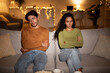 © Prostock-studio - In the evening, an unhappy couple sits apart on their sofa, arms crossed. They look distant after a conflict, highlighting difficulties in their relationship and feelings of misunderstanding.