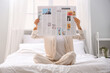 © Pixel-Shot - Young woman with newspaper sitting in bedroom
