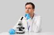 © Pixel-Shot - Thoughtful young male scientist with microscope sitting at table on grey background