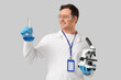 © Pixel-Shot - Young male scientist with microscope and chemical flask on grey background