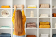 © Pixel-Shot - Young woman putting stack of clothes on shelving unit at home