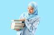 © Pixel-Shot - Beautiful young Asian woman in hijab with books on blue background