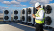 © Grispb - HVAC maintenance technician inspects rooftop cooling units, noting fan performance and system status to support efficient commercial climate control operations.