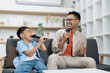 © itchaznong - Family Fun. Father and son enjoying karaoke at home, sharing laughter and joy.
