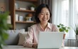 © hao - Happy mature middle aged Korean woman using laptop computer sitting at table in living room, hybrid working, elearning with technology at home, browsing internet, searching online. High quality
