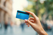 © vasyl pshyk - Holding a blue payment card in a busy street during the day in a city with blurred people in the background