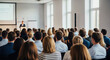 © abu - Diverse audience listens to a speaker during a business presentation in a sunlit conference room, focused on stage with the speaker.