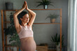 © NDABCREATIVITY - Charming pregnant fit woman in leggings and crop top exercising on yoga mat in living-room.
