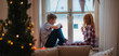 © Halfpoint - Small girl and boy sitting on window sill in pajamas. Christmas time.