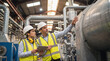 © alchena - Factory workers in yellow safety vests and white hardhats inspecting industrial plant. Two engineers pointing and discussing at manufacturing facility. Professional teamwork in production environment