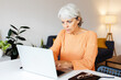 © Xavier Lorenzo - Senior businesswoman working on laptop computer sitting on table at home. Working at home and telecommuting concept