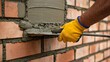© amanullahkhan - Worker applying cement mortar on brick wall during construction process