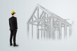 © Who is Danny - Architect in suit and yellow helmet observing sketched wooden house frame structure on light abstract background for construction planning concept.