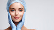 © GrayFrog - Young woman with a hairnet and blue gloves gently holds her face with copy space for beauty or cosmetic treatments.