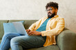 © Maria Vitkovska - Young man using laptop for remote work while sitting comfortably on sofa at home