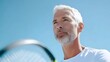© pkproject - Close up portrait of a focused senior athlete with silver hair and beard holding a tennis racket outdoors under a clear blue sky