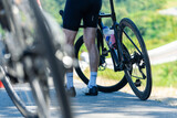 A cyclist pauses on the road, showcasing bike wheels and legs in cycling attire, with a scenic backdrop of greenery.