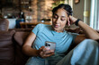 © Marko Geber - Young adult woman relaxed, using smartphone on couch at home