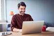 © baranq - Cheerful man laughing while working on laptop from home