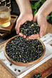 © HoangNam - Fresh Black Beans in Hands from Wicker Basket on Rustic Wood Table
