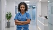 © Vasiliy - Confident black female doctor in blue scrubs posing in a hospital corridor. Portrait of a young african american nurse with a stethoscope and arms crossed. Healthcare and medicine professional