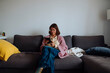 © teksomolika - Woman reclined on sofa cuddling small dog while browsing phone