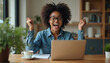 © Pete - Ecstatic Black woman celebrates winning something on laptop. Her arms are raised in joy. She wears glasses and a denim shirt. Success, good news, and achievement are evident.