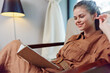 © SHOTPRIME STUDIO - Young woman reading a book in a cozy setting, wearing a brown linen dress and smiling, conveying joy and relaxation