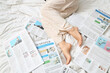 © Pixel-Shot - Legs of woman with newspapers on bed, top view