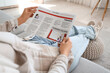 © Pixel-Shot - Young woman with newspaper sitting on sofa at home, closeup