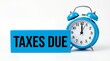 © Mary Patricia - Blue alarm clock shows approaching time next to a bright blue block with bold black text reading TAXES DUE representing urgency and deadlines finance financial money payment payment due