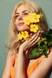 © VICHIZH - Bright beauty portrait of a model with flowing blonde hair holding vibrant yellow flowers against a soft green background, radiating warmth and positivity.