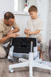 © Aboltin - Focused on assembling chair, adult instructs while child assists parts. Warm moment highlights family connection, patience, value of practicing useful skills together home. Boy screws screwdriver.