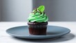 © ViskBx - Delicious chocolate cupcake with vibrant green mint frosting and a fresh mint leaf garnish on a blue plate, isolated on white background