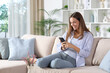 © Antonioguillem - Happy woman in blue using cell phone on a couch at home