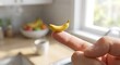 © Ziku - Hand holding a tiny miniature banana against a bright kitchen background