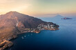 © AmazingAerialAgency - Aerial view of a rugged coastline meeting the tranquil sea, with a small village nestled along the shore, Panarea, Sicily, Italy.