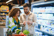 © Serhii - Couple checking grocery list in supermarket aisle