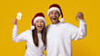 © Prostock-studio - A joyful couple wearing Santa hats smiles widely while holding a toy house and keys. Their excitement captures the festive spirit as they celebrate their new home during the holidays.