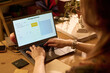 © pressmaster - Caucasian young adult woman typing on laptop using AI image generator software at wooden desk, hands on keyboard, digital workspace with office supplies and documents visible