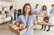 © Prostock-studio - A group of volunteers collects and sorts food donations in a community center. One young woman smiles while holding a box filled with food items. Others are busy preparing donations.