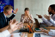 © Prostock-studio - In a tense corporate meeting, a group of coworkers shouts at a young businesswoman, pointing fingers and expressing frustration. She appears overwhelmed and covers her face with her hands.