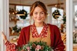 © Georgii - Woman in red cardigan holding a festive bouquet at a doorway, ready for Christmas gifts