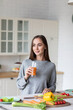 © BestForYou - Woman in a gray sweater is holding a glass of orange juice in a kitchen