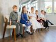 © JackF - Smiling little schoolchildren wearing elegant dresses sitting on chairs in school hall